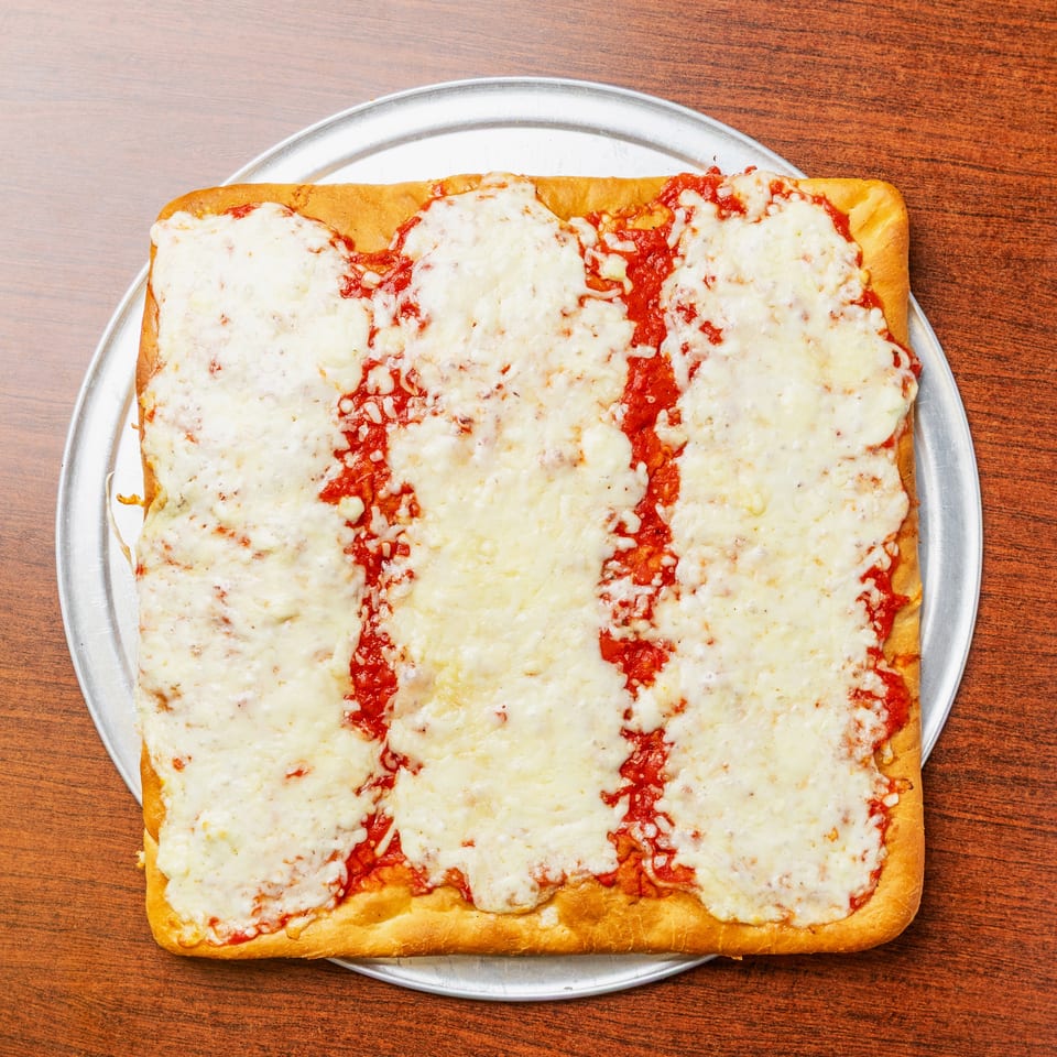 Rectangular cheese-covered pizza with tomato sauce on a metal tray atop a wooden table.