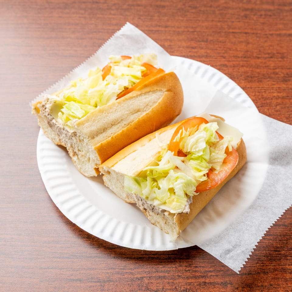 Two deli sandwiches with lettuce and tomato on a paper plate atop a wooden table.