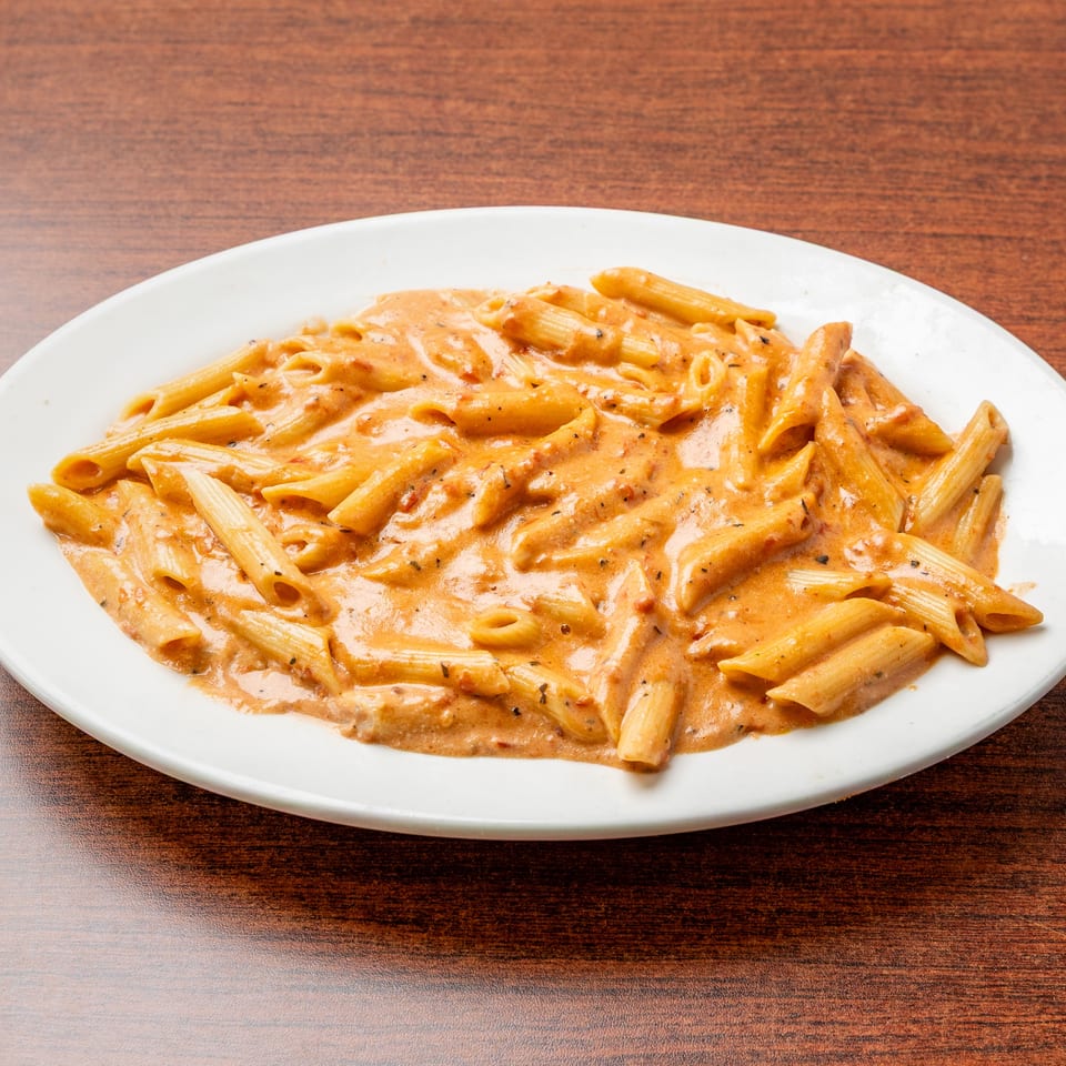 Penne pasta coated in creamy tomato sauce and herbs, served on a white plate atop a wooden table.