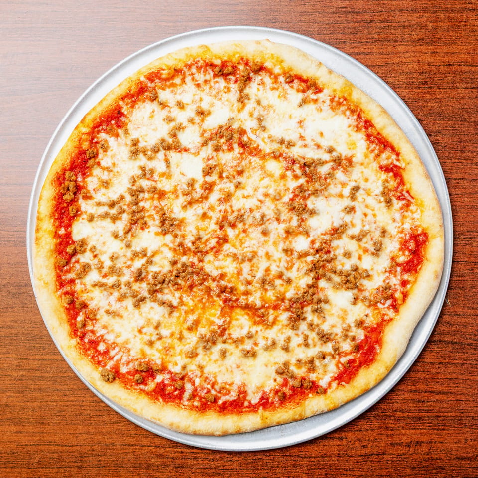 Large cheese and sausage pizza on a metal tray atop a wooden table.
