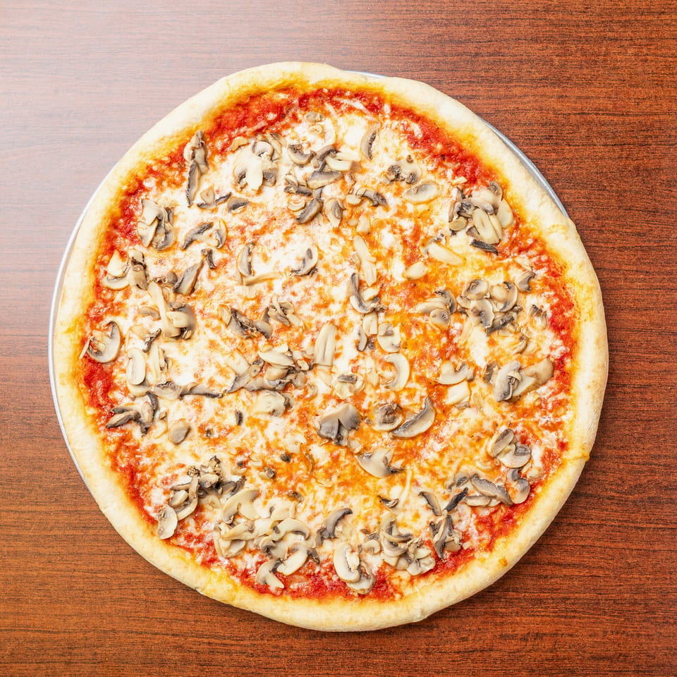 Round mushroom pizza with melted cheese and tomato sauce on a wooden table.