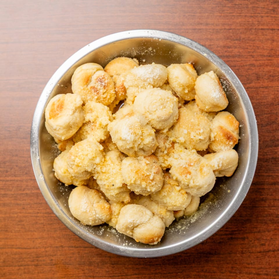 Metal bowl filled with golden, sugar-dusted pastries on a wooden tabletop.