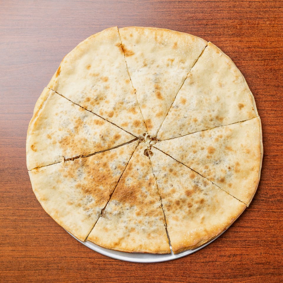 Large round stuffed flatbread cut into wedges on a metal tray atop a wooden table.