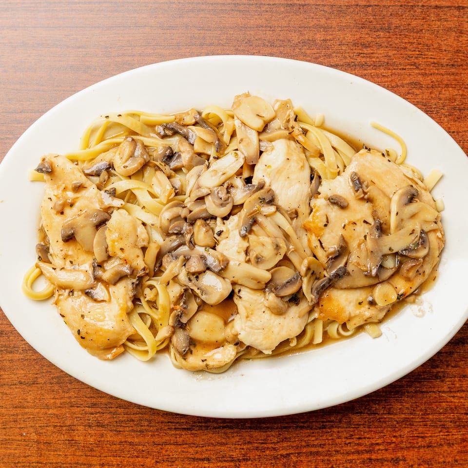 Chicken and mushroom fettuccine in a savory sauce, served on a white oval plate atop a wooden table.